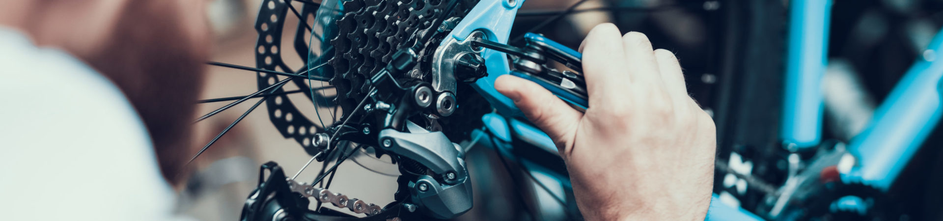 Bike Mechanic Repairs Bicycle in Workshop. Closeup Portrait of Young Blurred Man Examines and Fixes Modern Cycle Transmission System. Bike Maintenance and Sport Shop Concept